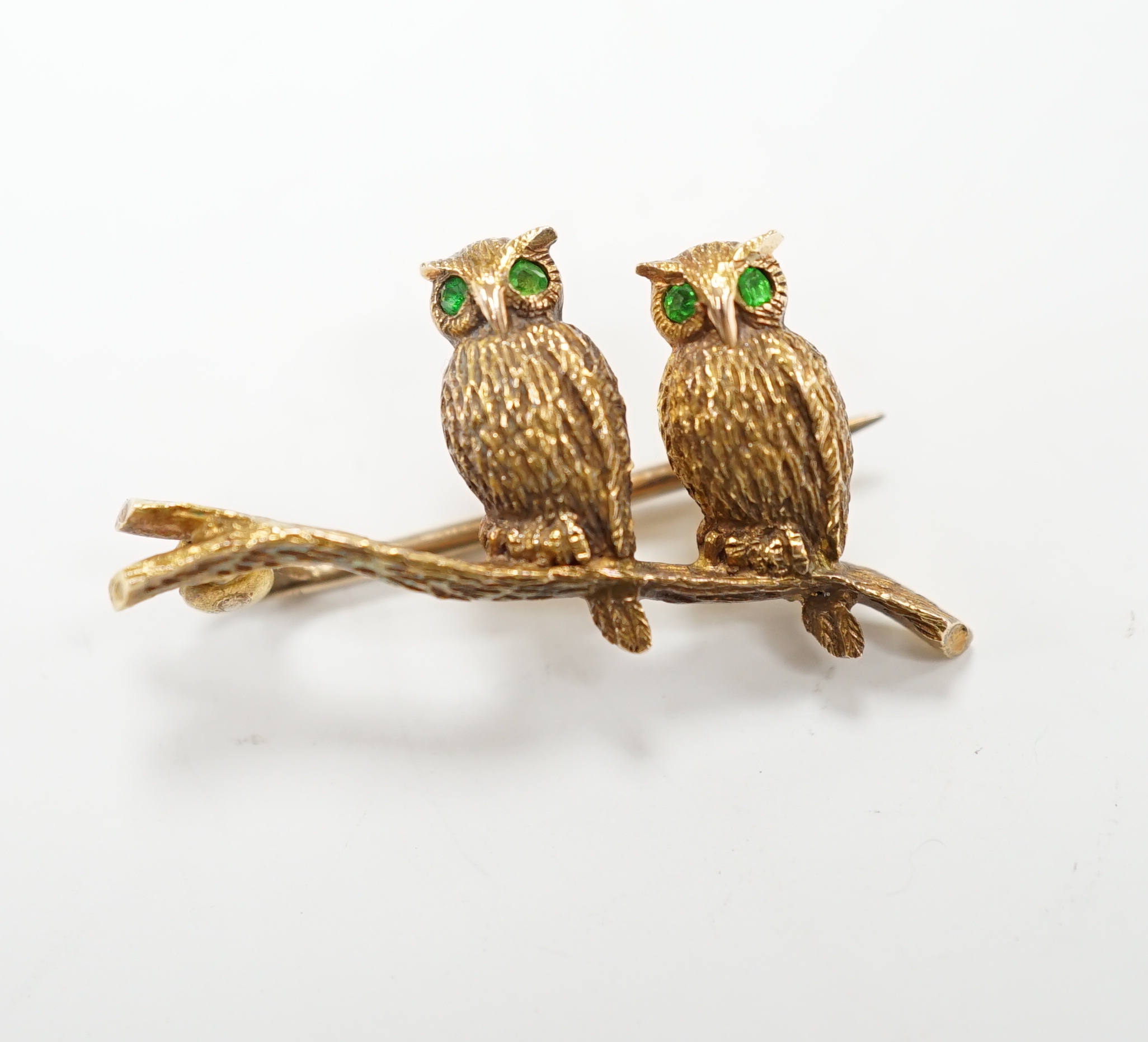 An Edwardian 15ct novelty brooch, modelled as two owls perched on a branch, with four stone green garnet set eyes, 26mm, gross weight 4.1 grams.